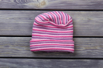 Pink woolen striped hat. Flat lay, top view. Dark wooden desk surface background.