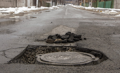Pothole in asphalt near the sewer hatch, in the middle of the street