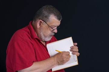 Nice low key portrait of a bearded senior writing a letter to his son in notebook