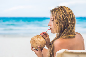 Young woman drinking coconut milk on Chaise-longue on beach.