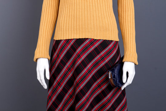 Front view sweater and checkered skirt. Mannequin with blue purse, black isolated background.