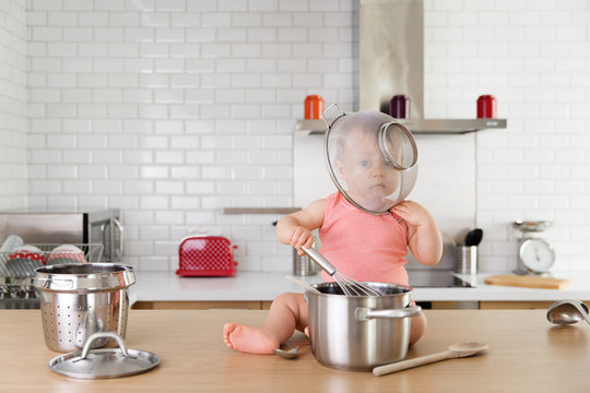 Baby boy playing on kitchen counter with strainer over his head