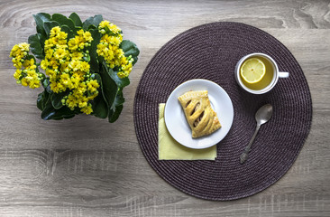 on a wooden background a flower of yellow color kalandive napkin round wicker tea cup lemon saucer puff croissant breakfast 