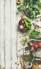 Winter vegetarian, vegan food cooking ingredients. Flat-lay of vegetables, fruit, beans, cereals, kitchen utencil, dried flowers, olive oil over white wooden background, top view, copy space, vertical