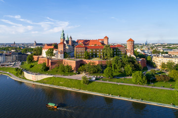 Krakow, Poland. Wawel hill with historic royal castle and cathedral, Vistula River, tourist boat, park and walking people. Aerial view in summer at sunset.