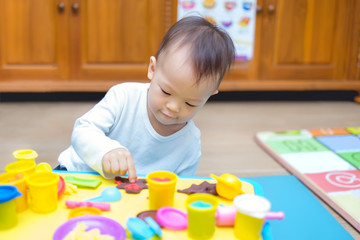 Cute little Asian 18 months old toddler baby boy child having fun playing colorful modeling clay / play dought, cooking toys in play room at home, Educational toys & Creative play for toddlers concept