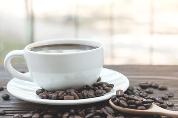 Black coffee in white cup surrounded by roast coffee bean.