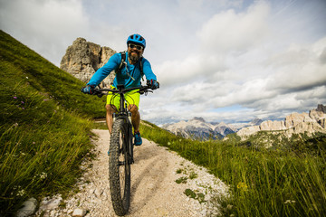 Fototapeta premium Tourist cycling in Cortina d'Ampezzo, stunning Cinque Torri and Tofana in background. Man riding MTB enduro flow trail. South Tyrol province of Italy, Dolomites.