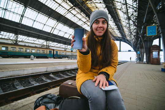 woman sit on her bags at railway station. show info on her phone