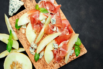 italian food with melon, prosciutto and cheese on cork cutting board