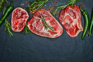 Raw juicy meat steaks ready for roasting and vegatables on a black board background. Space for text