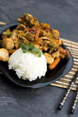 Fried vegetables with turkey meat and rice on the black plate. Asian delicates dishes with chili sauce.