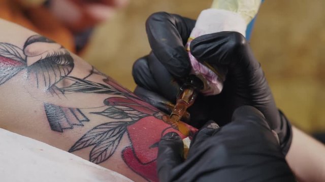 Macro view of professional tattoo master is painting with black ink, making shadow. Works in black latex gloves with handmade rotor gun machine in studio. 4k