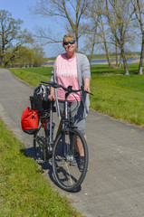 Woman standing on a bikeway beside her bike in rural surrounding near the Elbe River in the Lueneburg Heath at a sunny day with blue sky - portrait photo