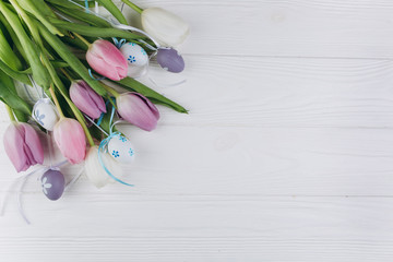 Easter bouquet with pastel colored eggs and tulips on a white wooden background.