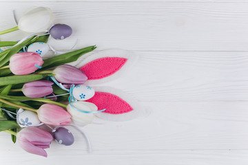 Obraz na płótnie Canvas Easter bouquet with pastel colored eggs, rabbit ears and tulips on a white wooden background.
