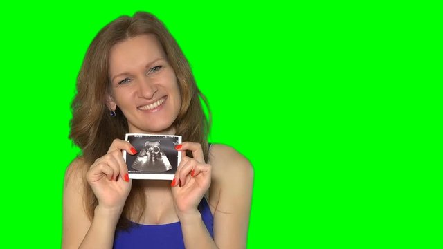 Happy young female showing her baby in tummy photo to camera and smile