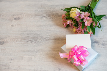 Obraz na płótnie Canvas Colorful spring bouquet of rose, chrysanthemum and alstroemeria flowers with empty card and gift box on wooden background