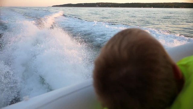 Slow motion of wake of large boat at sunset on the water and boy