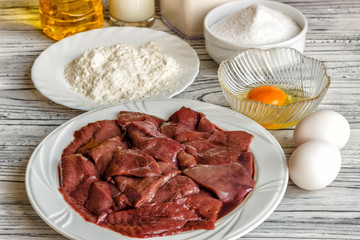 Raw liver on a white plate on a wooden background. A set of products for cooking fried liver egg oil salt flour. Food ingredient. Selective focus.