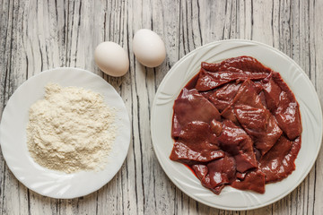 Raw liver on a white plate on a wooden background. A set of products for cooking fried liver egg oil salt flour. Food ingredient. Selective focus.