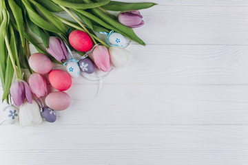 Easter composition with colored eggs and tulips on a white wooden background.