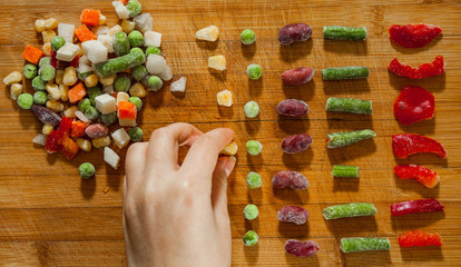 woman's hand collects even row of colorful Frozen mixed vegetables on a wooden background. top view