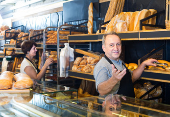polite mature bakers with fresh bread in bakery