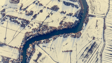 Aerial view riverbend passing snow covered fields.