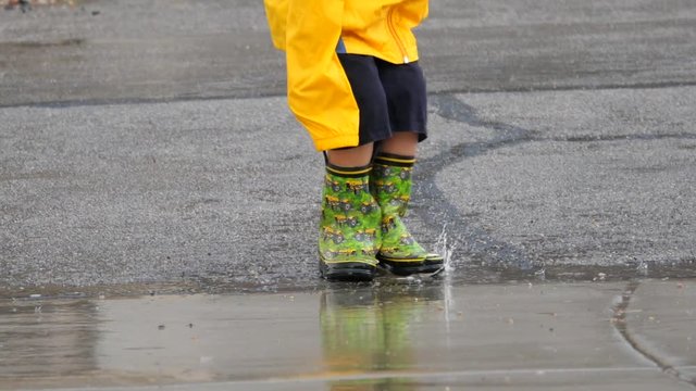Slow motion shot of a boy playing in a rain storm puddles with boots