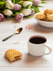 Coffee Cup with biscuits and tulips on a wooden table