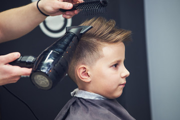 Hairdresser making a hairstyle to a boy in barbershop. - 196065432