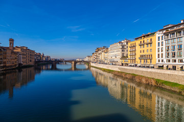 Fototapeta na wymiar Cityscape view on Arno river with famous Holy Trinity bridge in Florence. Reflections on water. Old colorful houses on the side. Tuscany, Italy