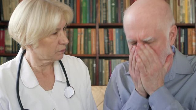 Female professional doctor in white coat with stethoscope at work. Senior woman physician talking to sick coughing badly senior male patient at home consulting about treatment and therapy options