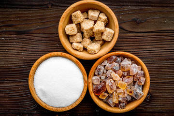 Sugar background on dark wooden table. Bowls with different kinds of sugar. Top view