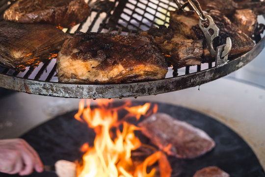 Delicious Crusty Pork Roast On A Bbq Grill, The Grillmaster Is Taking Care Of The Charcoal Fire Underneath