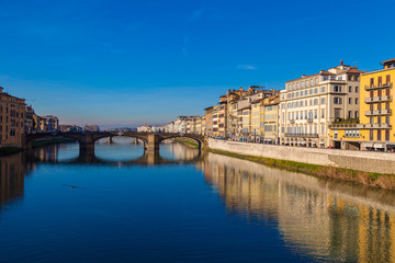 Fototapeta na wymiar Cityscape view on Arno river with famous Holy Trinity bridge in Florence. Reflections on water. Old colorful houses on the side. Tuscany, Italy