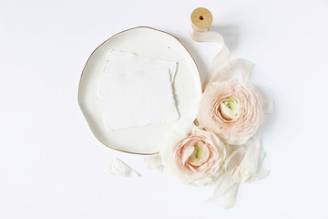 Feminine wedding, birthday desktop mock-up scene. Porcelain plate, blank craft paper greeting cards, silk ribbon, blush pink Persian buttercup flowers. White table background. Flat lay, top view.