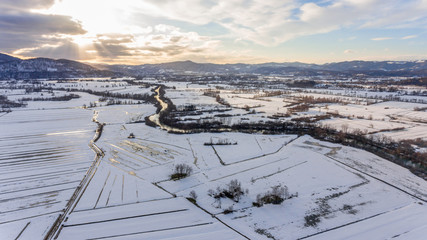 Aerial view of river flowing through snow covered countryside at sunset.