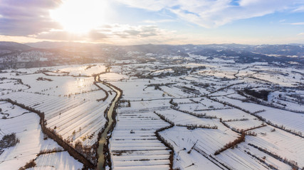 Obraz premium Aerial view of river flowing through snow covered countryside at sunset.