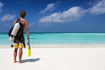 Scuba Taucher mit Ausrüstung steht am Strand und schaut auf den Ozean