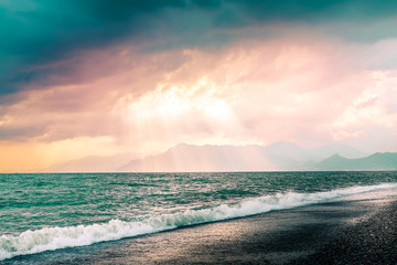 Obraz premium Beautiful summer seascape with mountains silhouette. Cloudy pink sky with sunrays through clouds. Salerno beach, Italy