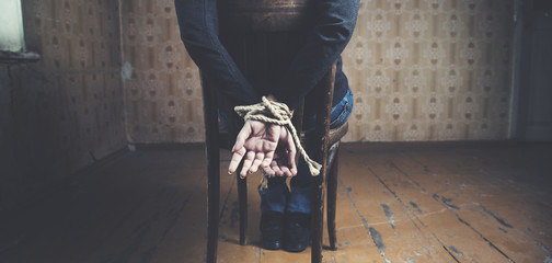 young woman tied to chair on dark background