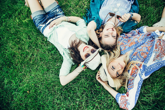 Trendy Hipster Girls Relaxing on the Grass . Summer lifestyle portrait of three hipster women laying on the grass enjoy nice day, wearing bright sunglasses. Best friends girls having fun, joy.
