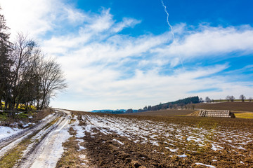 Straw bales and manure on the countryside field. Spring fields and preparation for agriculture. Typical czech countryside land, trees and blue sky