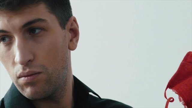 Suspicious man raises and looking at red women's bra. Man finds a bra and takes it. A man in a black shirt in the morning in home finds and looks at a red female bra with surprise