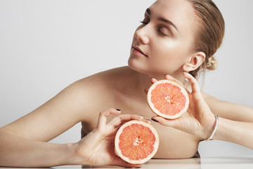 Close up portrait the blonde woman holding half an orange isolated on the white background.