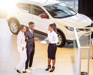 High angle view of african car saleswoman standing at dealership telling about features of car to...