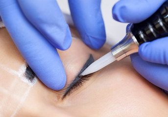 Permanent make-up for eyebrows of beautiful woman with thick brows in beauty salon. Closeup...