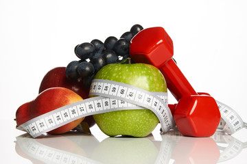 Fitness equipment and healthy food isolated on white. Red dumbbells with fresh fruit and green...